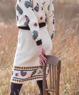 Sweater de punto color marfil con bordados artesanales en relieve de motivos paisley y florales en tonos morados, celestes y marrones. Posee cuello alto, puños y dobladillo en tono marrón oscuro.
