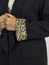 Blazer negro de corte clásico con solapas redondeadas y bolsillos con solapa. Presenta un detalle distintivo de estampado animal print en el interior de los puños, visible al doblar las mangas.