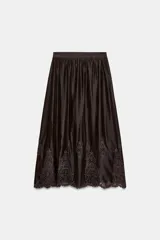 Falda midi marrón oscuro, con diseño fluido y voluminoso, tiro alto y detalles de bordados a tono en el ruedo.