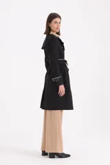 Piloto 7/8 de corte trench, color negro con detalles en beige en cuello, solapas y puños. Presenta cierre cruzado con botones, cinturón con hebilla y charreteras en los hombros.