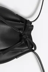 Bolso tipo bucket pequeño de piel vacuna, color marrón, con estructura blanda. Cuenta con asa regulable de piel y cierre de cordón ajustable. Presenta el logo metálico de BIMBA Y LOLA en dorado.