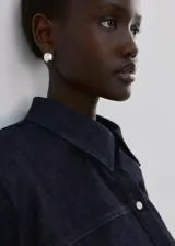 Camisa de denim azul oscuro, con cuello camisero, cierre frontal con botones y mangas largas ajustadas.