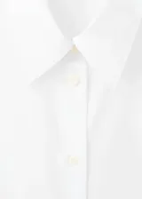 Camisa de popelín color blanco, de manga larga, con cierre frontal de botones y cuello camisero con solapa.