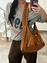 Bolso marrón de cuero con remaches metálicos plateados. Tiene correa larga para usar cruzada o al hombro, bolsillo interior y argolla para colgar accesorios.