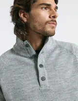 Sweater de punto color azul marino, con cuello alto, cierre frontal parcial y tapeta con botones. Presenta mangas raglán y puños y ruedo acanalados.