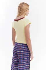 Top de canalé amarillo con cuello redondo y ribetes en color bordo, mangas cortas y detalle de logo bordado en el pecho.