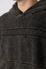 Buzo canguro de corte oversize en color gris con efecto lavado desgastado. Presenta diseño con recortes horizontales, capucha amplia y puños acanalados con etiqueta de marca en la manga.