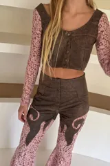 Top corto confeccionado en cuero negro con mangas largas de encaje floral. Presenta escote en V, diseño entallado con costuras decorativas y cierre frontal mediante botones metálicos.