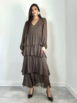 Vestido largo de seda italiana color chocolate, con escote en V, mangas largas abullonadas y diseño de múltiples volados horizontales que aportan volumen y movimiento.