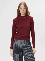 Polera de manga larga confeccionada en tela rib color bordó, con cuello alto y hombreras. Presenta costuras a la vista con pespuntes en hilo de color contrastante en el cuello, puños, hombros y ruedo.