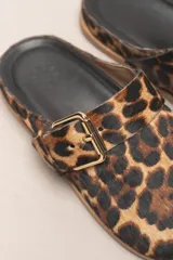 Zueco destalonado de cuero vacuno con estampado de leopardo. Presenta una tira ancha con hebilla metálica dorada sobre el empeine.