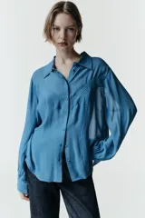 Camisa de manga larga con cuello solapa, confeccionada en tejido fluido. Presenta detalle de jaretas verticales en el frente y cierre frontal con botones forrados al tono.