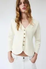 Chaqueta de punto color negro, con escote en pico, manga larga y cierre frontal con botones dorados. Presenta un diseño con bajo asimétrico.