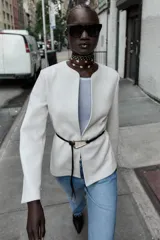 Blazer de textura suave, cuello redondo y manga larga. Presenta un diseño minimalista con cierre frontal mediante un cinturón fino de cuero con hebilla metálica.