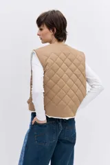Chaleco reversible de diseño acolchado con costuras en rombos, color tostado con interior de corderito blanco. Presenta cierre frontal con botones, cuello redondo y bolsillos delanteros.