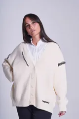 Cárdigan color crema de tejido de punto, con cuello en V, cierre frontal con botones y diseño oversize con bordados de costuras en negro.