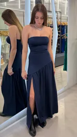 Vestido largo azul marino strapless con escote recto, corte ajustado en el torso y falda larga con tajo lateral profundo y detalle de volados en la parte inferior.