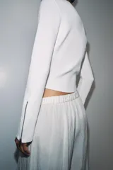 Chaqueta de punto liso color blanco, con cuello redondo, manga larga acabada con cremalleras en los puños y cierre frontal con cremallera.