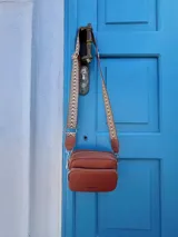 Bandolera de símil cuero color verde oliva, con diseño de dos compartimentos con cierre y correa ajustable de tela con patrón geométrico.