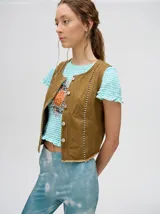 Chaleco de denim liviano con cierre frontal de botones metálicos, detalle de apliques metálicos verticales y ruedo con terminación desflecada.