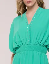 Vestido largo amarillo de corte fluido con escote en V, mangas cortas amplias y apliques de tachas en el escote y puños. Posee cintura elastizada fruncida y falda larga con tajos laterales en el ruedo.