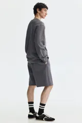 Short de felpa interlock color gris oscuro, con cintura elástica fruncida y cordón ajustable. Presenta un diseño de corte relajado a la rodilla, bolsillos laterales y bolsillos traseros.