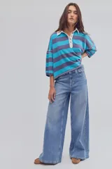 Remera tipo polo de algodón, de calce oversize, con cuello clásico blanco, botonadura corta, hombros caídos y diseño a rayas horizontales azules y celestes.