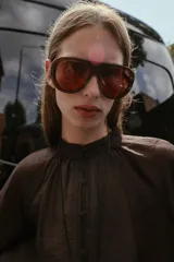 Blusa de cuello subido y manga larga abullonada con puños ajustados. Presenta un diseño semitransparente con textura arrugada y cierre frontal con botones a tono.