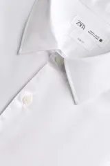 Camisa de manga larga, color blanco, con cuello italiano y corte slim fit. Presenta cierre frontal de botonadura y puños con botón.