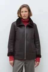 Chaqueta de eco cuero color chocolate con interior y cuello forrados en piel sintética al tono. Presenta cierre frontal completo, bolsillos laterales y diseño de corte recto.
