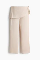 Pantalón de satén color beige con diseño de pierna recta y pollera mini cruzada superpuesta con tiras finas decorativas en un lateral.