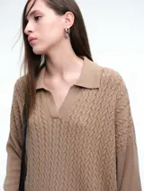 Sweater de tejido de punto color beige, con diseño de trenzas en el frente y mangas lisas. Presenta cuello polo con escote en V y puños y ruedo acanalados.