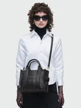 Cartera tipo tote de cuero rojo de la marca Marc Jacobs, modelo The Leather Small Tote Bag. Presenta doble asa superior, correa ajustable y extraíble para el hombro, y el texto grabado en relieve "THE TOTE BAG MARC JACOBS" en el frente.