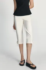 Pantalón capri de tiro alto en color crudo, con detalle de lazos ajustables en los bajos y cierre lateral con cremallera oculta.