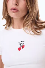 Remera de algodón color blanco, de corte ajustado y manga corta, con cuello redondo y estampa pequeña en el centro del pecho con forma de corazones y texto.