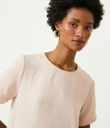 Blusa blanca de poliéster de corte recto, con cuello redondo, mangas cortas con dobladillo y detalles de pespuntes a contratono.