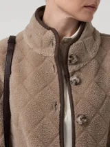 Chaqueta de polar color beige con diseño acolchado de rombos y ribetes en contraste. Presenta cierre frontal de botones, cuello alto, manga larga y bolsillos delanteros aplicados. Confeccionada en poliéster reciclado con detalles de cuero.