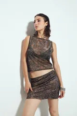 Top sin mangas ajustado al cuerpo, con escote cerrado. Presenta un tejido liviano y transparente con estampado damasco en tonos negro y marrón/bronce, que deja ver la ropa interior oscura que se lleva debajo.