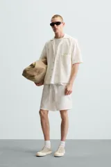 Bermuda de algodón color blanco, de corte relajado (relaxed fit), con cintura elástica ajustable mediante cordón. Posee bolsillos laterales y un bolsillo trasero de plastrón. Presenta un bordado en contraste en la pernera.