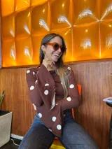 Blusa de manga larga ajustada al cuerpo, color marrón con estampado de lunares blancos. Presenta un cuello redondo con caída suave y mangas acampanadas con volados en los puños.