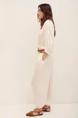 Pantalón de satén color marfil, de tiro medio con elástico en la cintura, bolsillos laterales y puños elásticos en los tobillos.