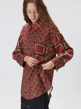 Camisa de seda con cuello camisero, manga larga y bolsillo frontal. Presenta un diseño estampado geométrico de cuadrados en tonos marrones y azul oscuro.