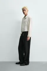 Camisa de corte relajado confeccionada en tejido fluido con textura jacquard de rayas verticales. Presenta cuello clásico, cierre frontal con botones, manga larga con puños abotonados y un bolsillo de parche en el pecho.