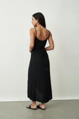 Vestido negro midi de tirantes finos, con escote cruzado en V y diseño envolvente con drapeado lateral que genera una abertura frontal.