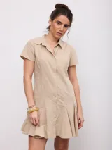 Vestido corto beige de corte camisero, con cuello solapa, mangas corta y cierre frontal con botones a presión. Cuenta con falda evasé con pliegues.