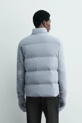 Chaleco acolchado de corte regular, confeccionado en tejido técnico con relleno de plumón. Presenta cuello subido, cierre frontal con botones a presión y dos bolsillos frontales de plastrón con solapa.