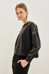 Buzo de algodón color negro con efecto lavado, corte holgado y detalles de tachas metálicas plateadas alrededor del cuello redondo y en los hombros.
