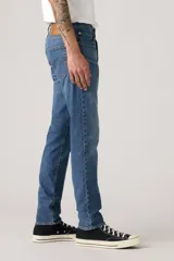 Pantalón de jean corte slim taper, con diseño de cinco bolsillos, cierre de cremallera y botón metálico, en tono azul medio con efecto lavado.