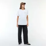 Camiseta de lactancia blanca de manga corta, con cuello redondo y estampa frontal con texto y diseño de tablero de ajedrez. Presenta aberturas laterales discretas para facilitar la lactancia.