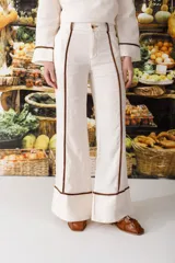 Pantalón de vestir color manteca, de corte recto y tiro alto, con detalle de ribetes marrones en los laterales.